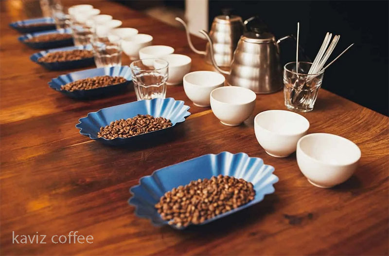 میز حاوی انواع قهوه و فنجان ها و قاشق و کتری برای blind cupping